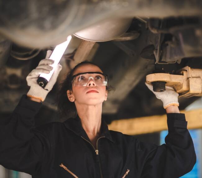 car mechanic standing under car in garage inspecting and doing maintenance work for car