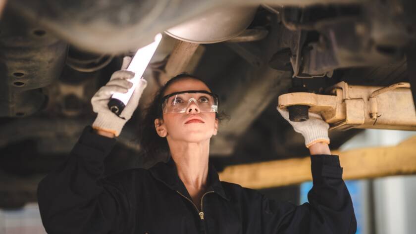 car mechanic standing under car in garage inspecting and doing maintenance work for car