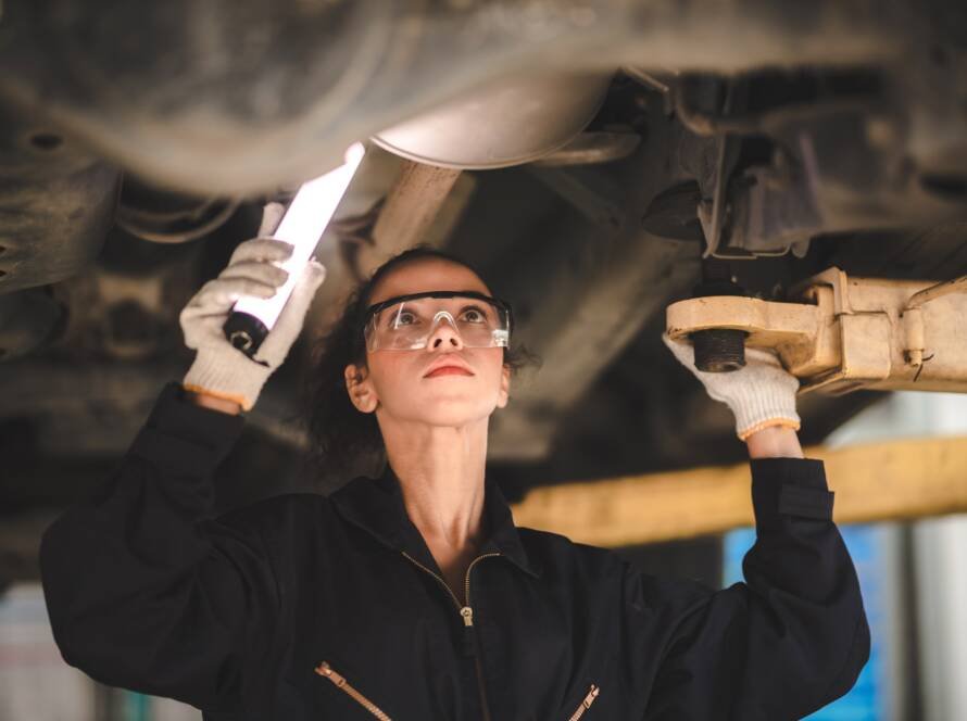car mechanic standing under car in garage inspecting and doing maintenance work for car